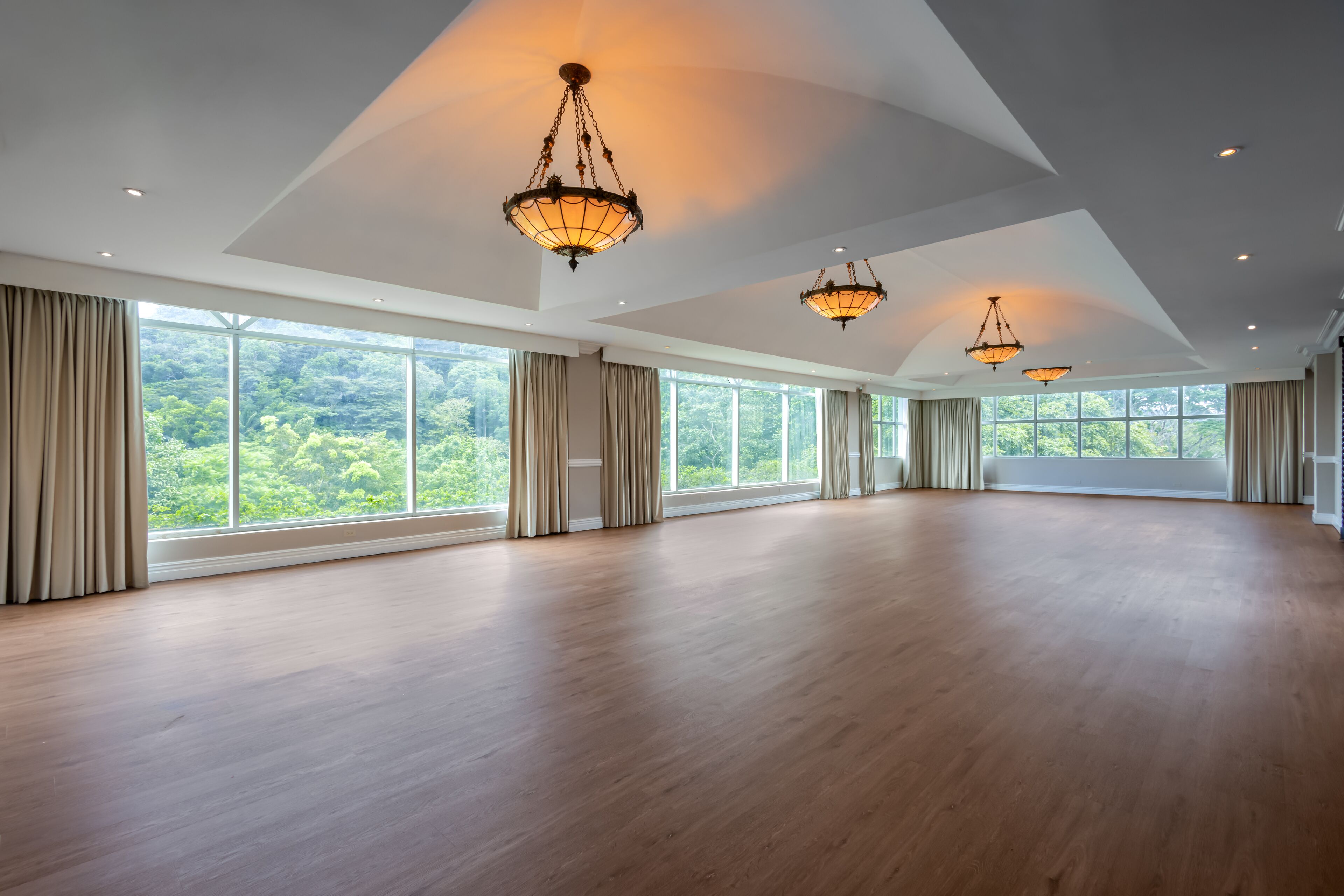 A spacious room with large windows, wooden flooring, and hanging chandeliers.