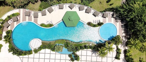 Vista aérea de un resort con una gran piscina, tumbonas y palmeras.