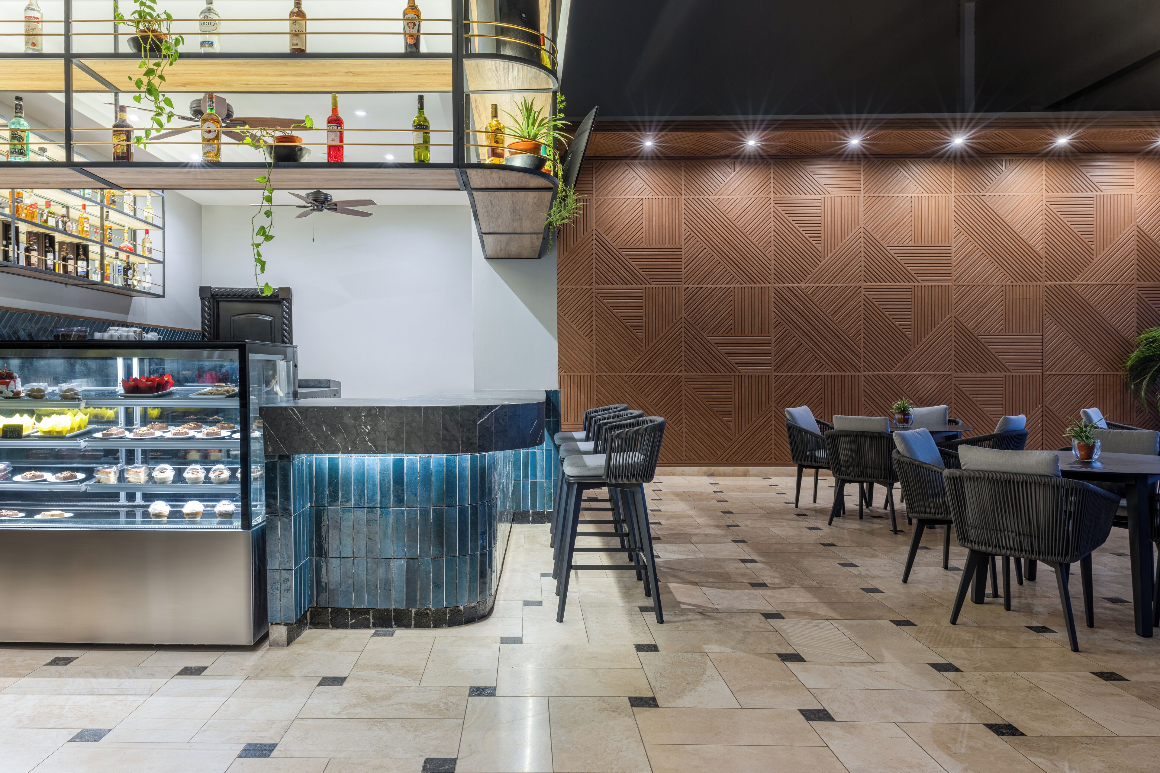 Eine moderne Bar mit einer Dessertvitrine, einer Sitzgelegenheit mit Stühlen und Tischen sowie einer Wand mit Muster und einem Deckenventilator.