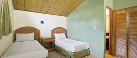 Une chambre avec deux lits simples, un ventilateur de plafond en bois et un mur vert.