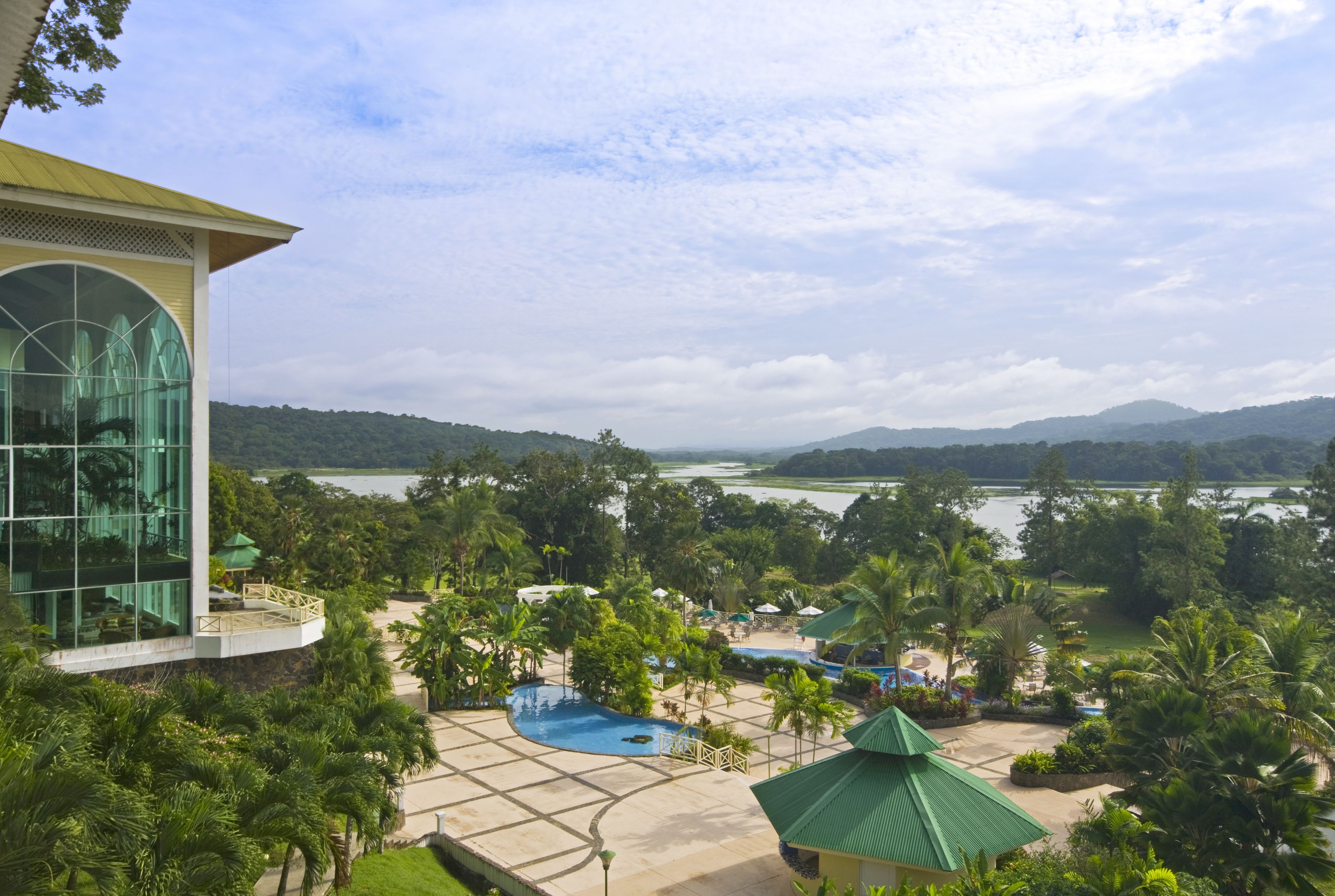 A resort with a large glass building, a swimming pool, and a view of a lake and mountains.