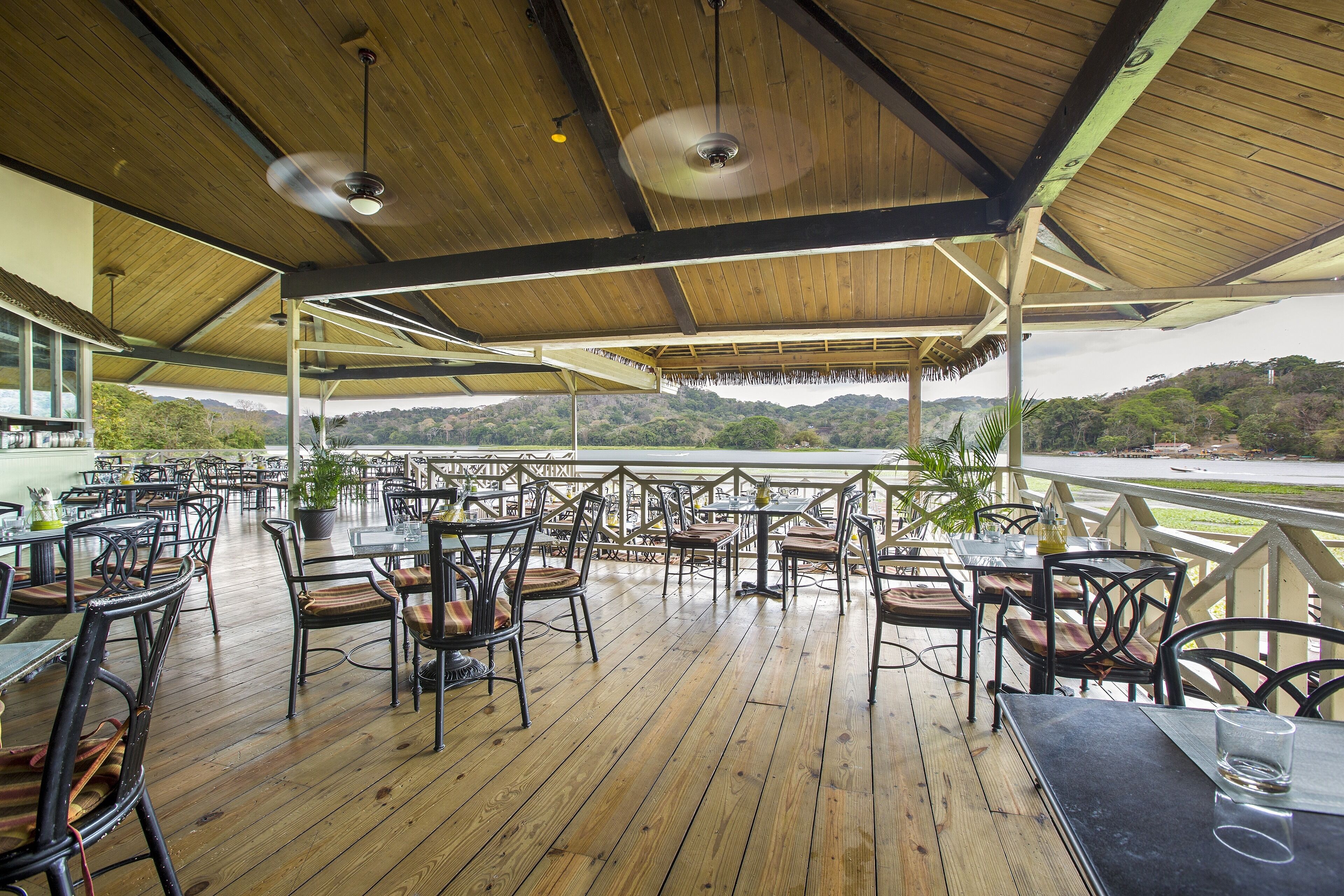 Un área de comedor al aire libre con piso de madera y sillas de metal, con vistas a un paisaje pintoresco.