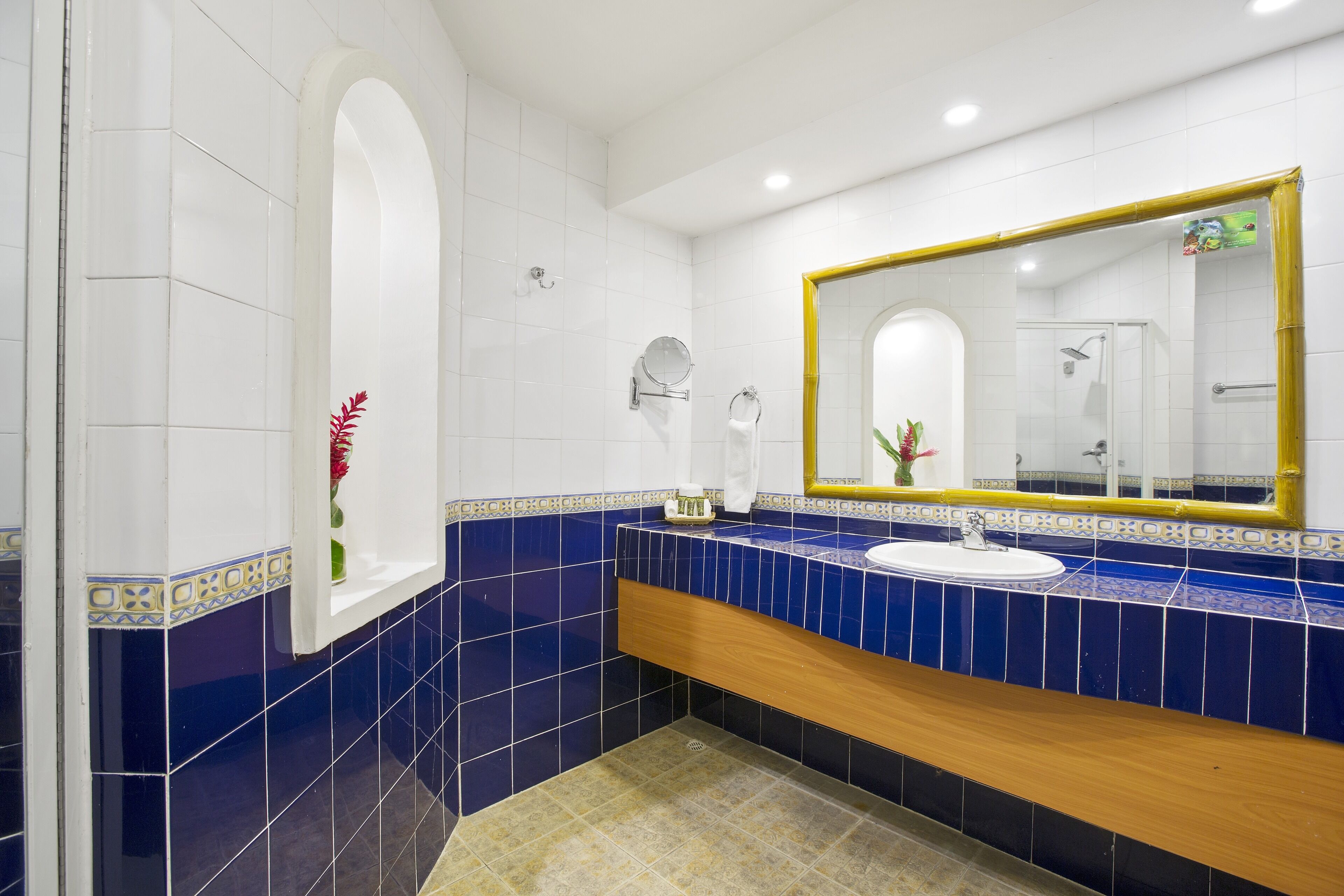 Un baño con un lavamanos blanco, azulejos azules, un mueble de tocador de madera y un espejo grande con marco dorado.