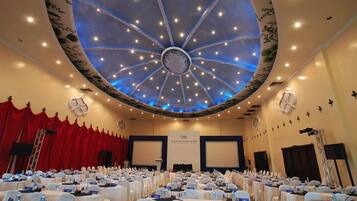 Een congrescentrum met een rond plafondontwerp, meerdere tafels met naambordjes, en een podium aan de voorzijde.