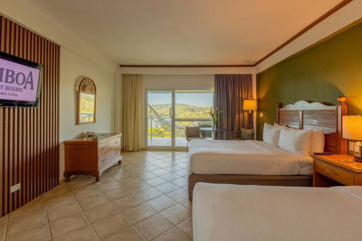 A hotel room with two beds, a TV, a desk, and a view of a balcony.