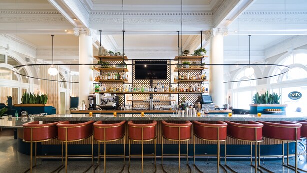 A bar area with a long counter, multiple stools, and shelves stocked with bottles. - Hotel Shattuck Plaza (Berkeley)