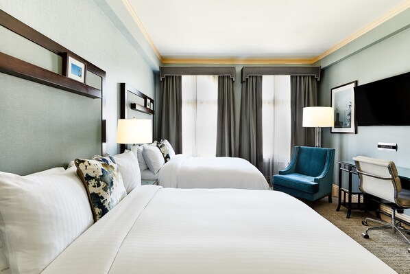 A hotel room with a large bed, two bedside tables, a desk with a chair, and a TV mounted on the wall.