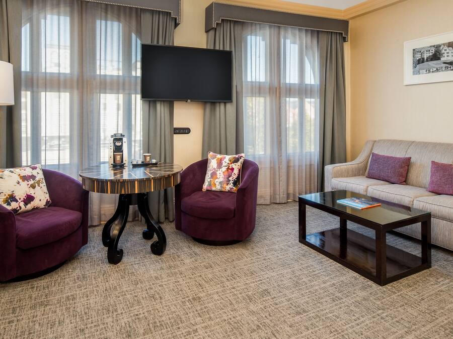 Een hotelkamer met een bank, twee fauteuils, een bijzettafeltje, een televisie en een schilderij aan de muur.