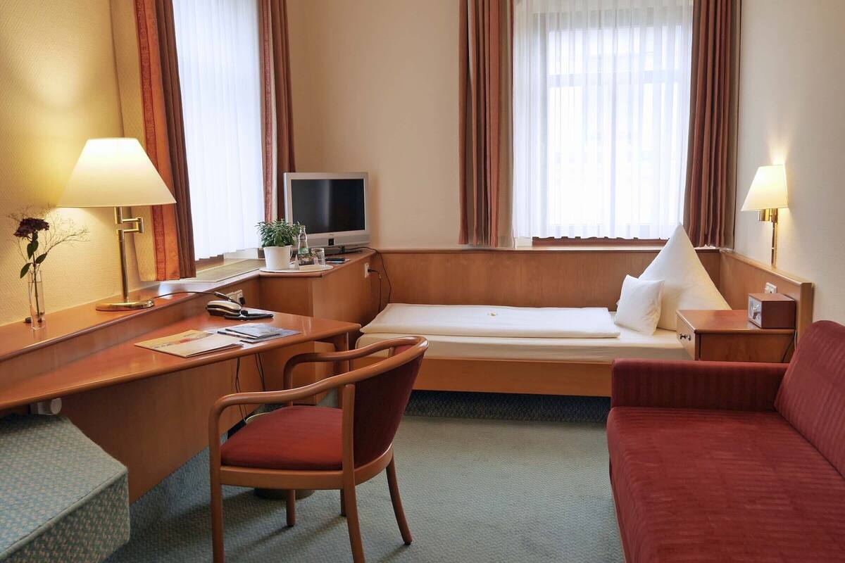 A hotel room with a bed, a desk with a chair, a TV, and two lamps.