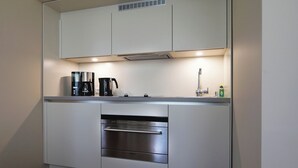 A compact kitchen with white cabinetry, a built-in oven, a coffee maker, and a kettle. - Hotel Martha Dresden (Dresden)