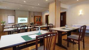 A conference room with multiple tables and chairs, a projector screen, and a cabinet with glass doors. - Hotel Martha Dresden (Dresden)