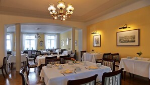 A dining area with multiple tables set for service, wooden chairs with patterned upholstery, and a chandelier. - Hotel Martha Dresden (Dresden)