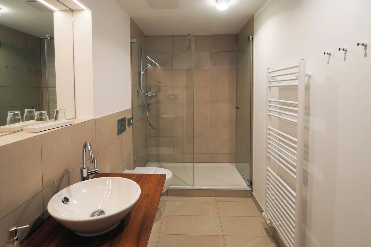 A modern bathroom with a glass shower enclosure, a white sink with a wooden countertop, and a white radiator.