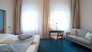 A hotel room with a bed, a sofa, a chair, a small table with a lamp, and curtains. - Hotel Martha Dresden (Dresden)