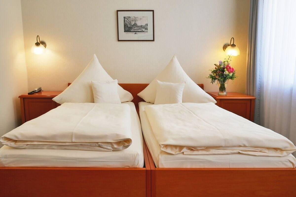 A double bed with white linens in a hotel room.