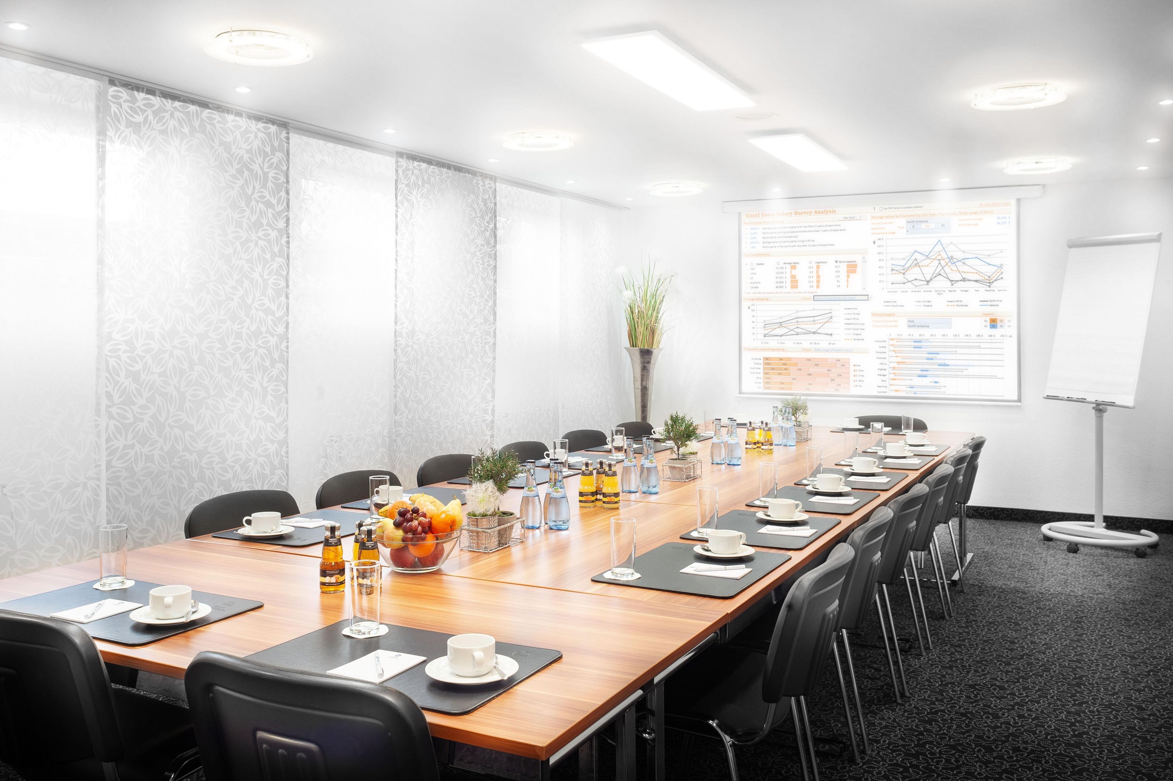 A conference room with a long table, chairs, a whiteboard, and presentation screens.