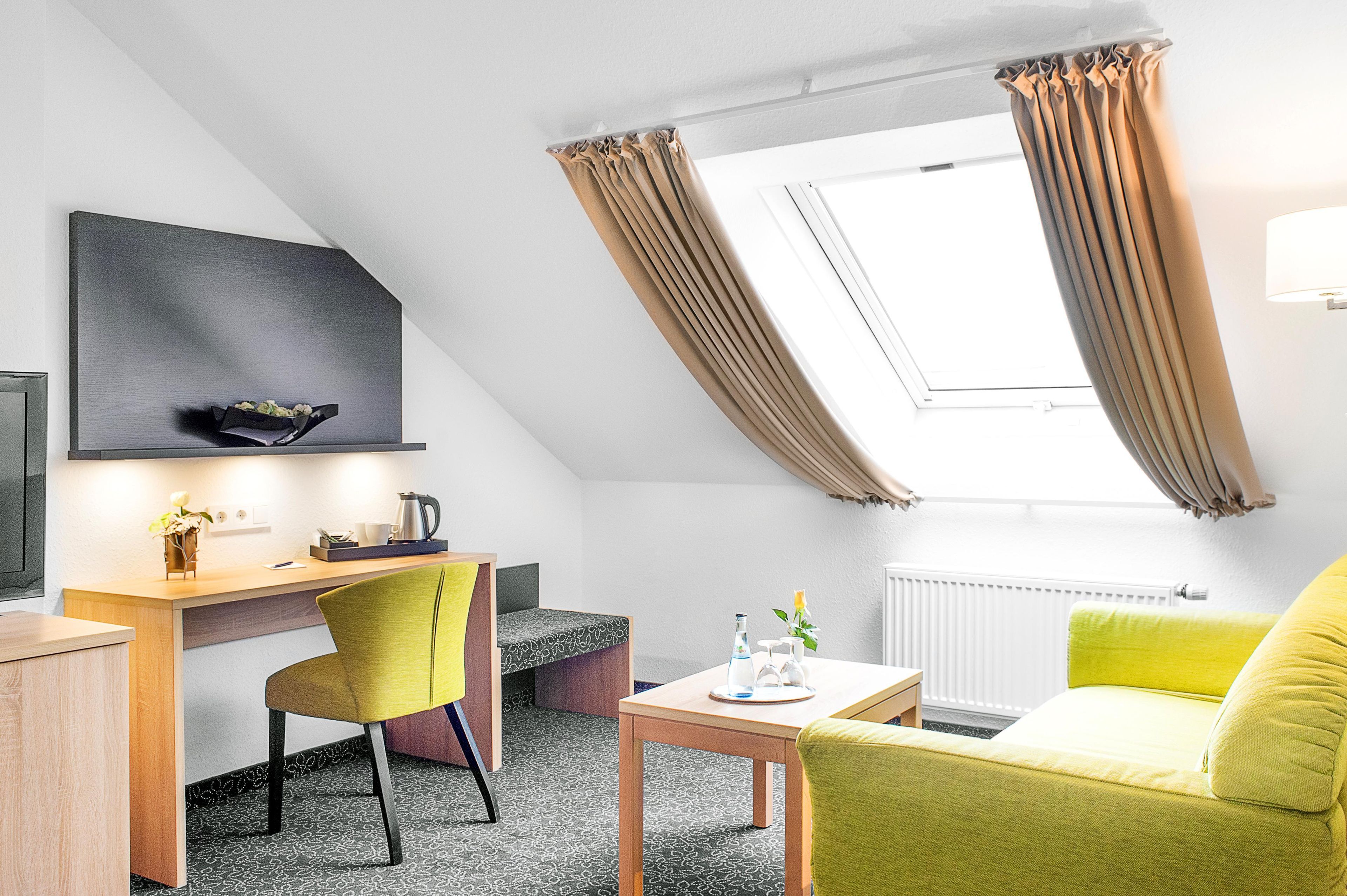 Ein modernes Zimmer mit Schreibtisch, Stuhl, Sofa und einem Fenster mit Vorhängen.