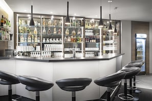 Eine moderne Bar mit einer zentralen Theke, Barhocker und einer Auswahl an Spirituosenflaschen und Gläsern.