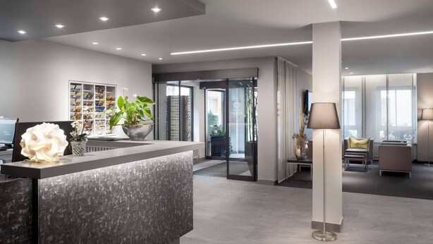 A modern reception area with a reception desk, a potted plant, and a large decorative light fixture. - Best Western Hotel Favorit (Ludwigsburg)