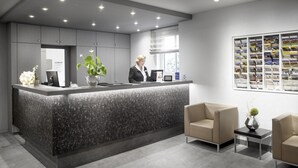 A reception desk with a receptionist, a plant, and a wall with brochures. - Best Western Hotel Favorit (Ludwigsburg)