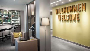 A modern reception area with a 'WILLKOMMEN WELCOME' sign, a bar with various bottles, and seating with a lamp. - Best Western Hotel Favorit (Ludwigsburg)
