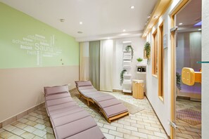 A spa room with two massage tables, a wall with wellness-related words, and a sliding glass door leading to another area. - Best Western Hotel Favorit (Ludwigsburg)