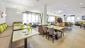 A modern dining area with multiple tables and chairs, a central counter, and large windows allowing natural light. - Best Western Hotel Favorit (Ludwigsburg)