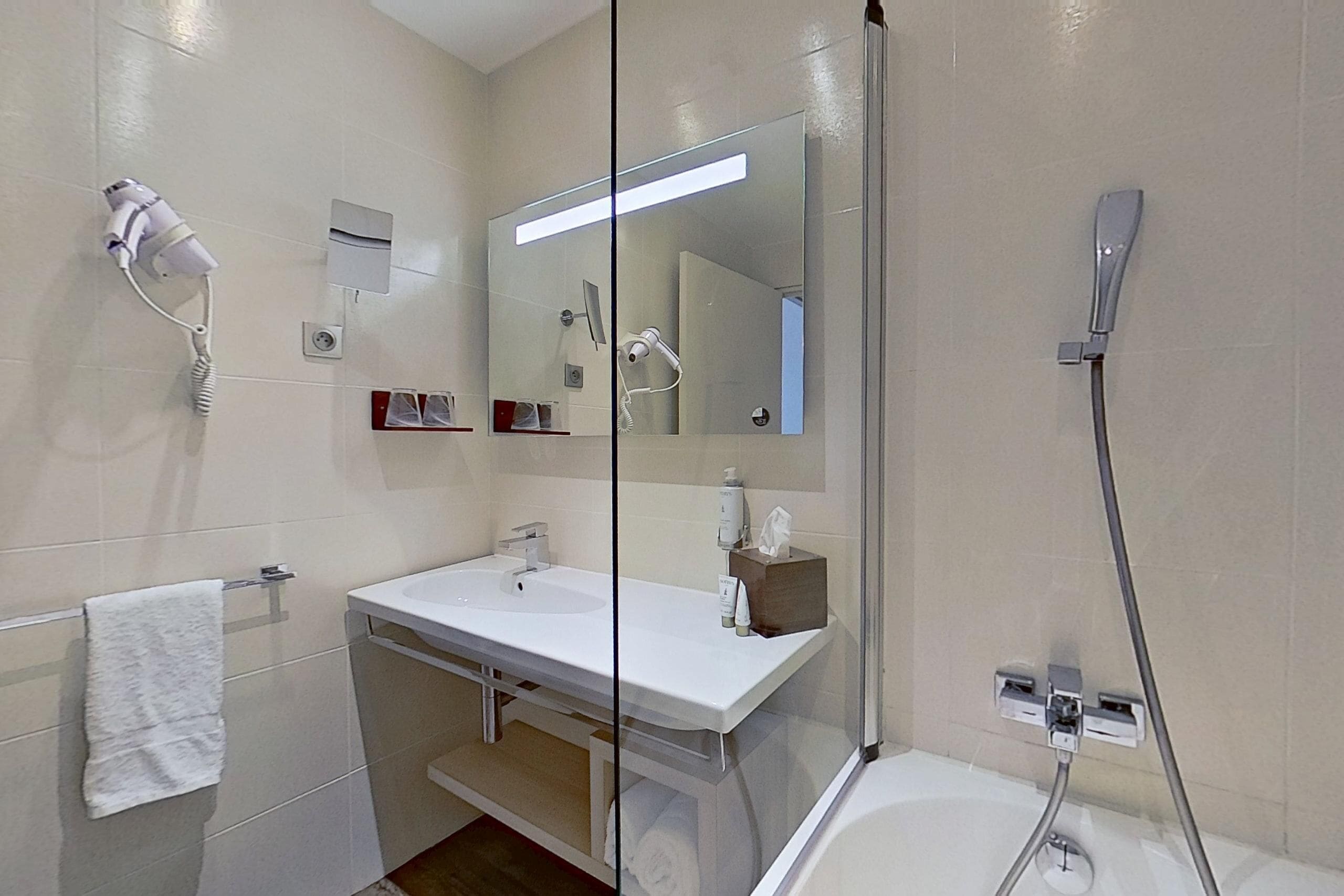 Un baño moderno con cabina de ducha de vidrio, un lavamanos blanco y un secador de pelo montado en la pared.