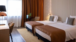 A hotel room with two beds, a desk, a chair, a lamp, and a window with curtains. - Aquabella Hôtel & Spa (Aix-en-Provence)