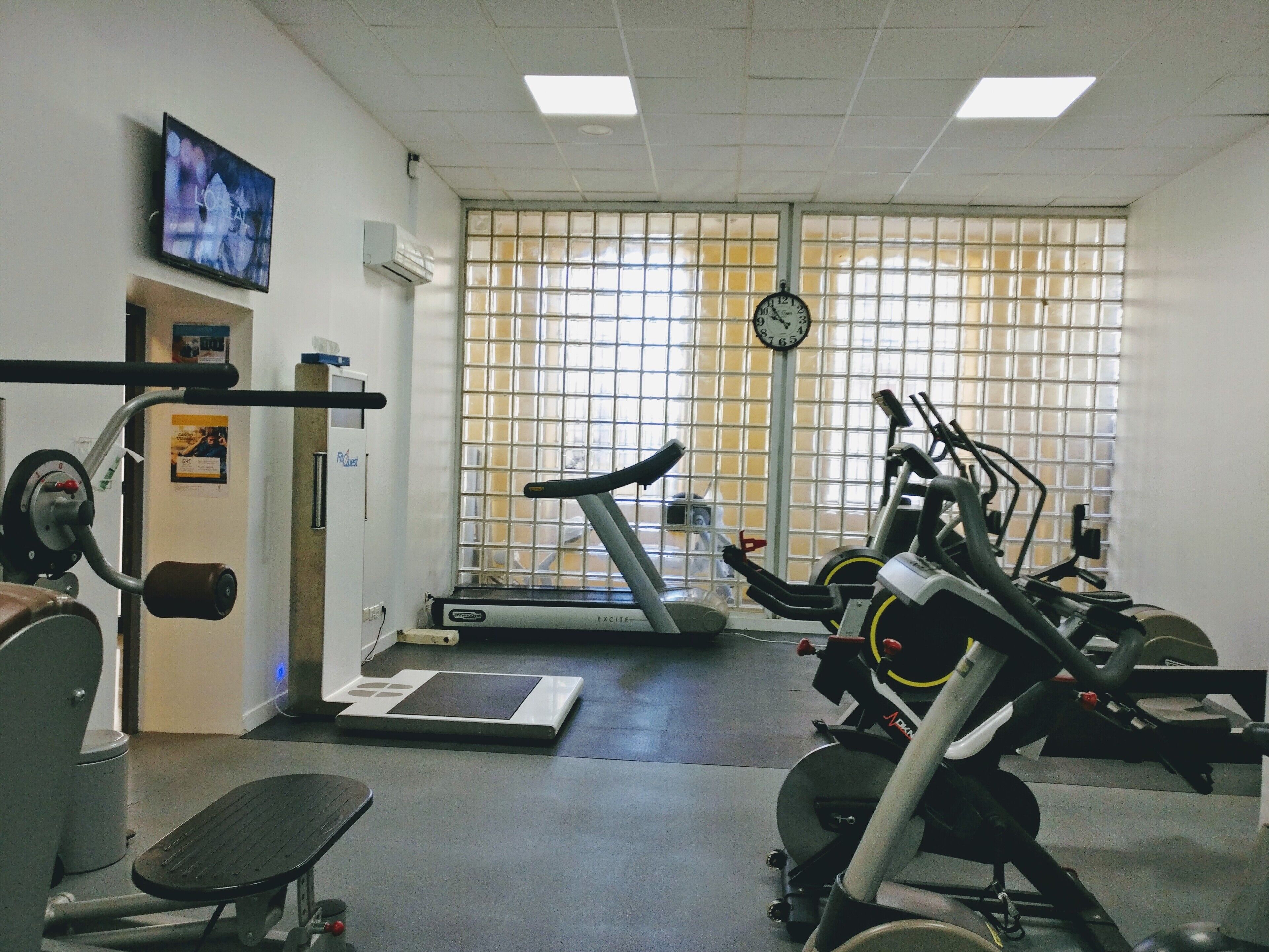 Un gimnasio con equipo de ejercicio, una cinta de correr y un reloj en la pared.