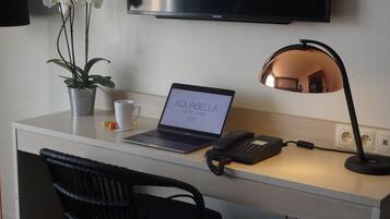 Habitación de hotel con escritorio, computadora portátil, teléfono, lámpara, planta y televisor.