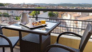 A balcony with wicker chairs, a table with breakfast items, and a city view. - Aquabella Hôtel & Spa (Aix-en-Provence)