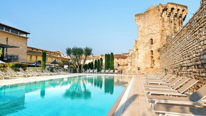 A swimming pool with lounge chairs, a stone wall, and a building with a tiled roof. - Aquabella Hôtel & Spa (Aix-en-Provence)
