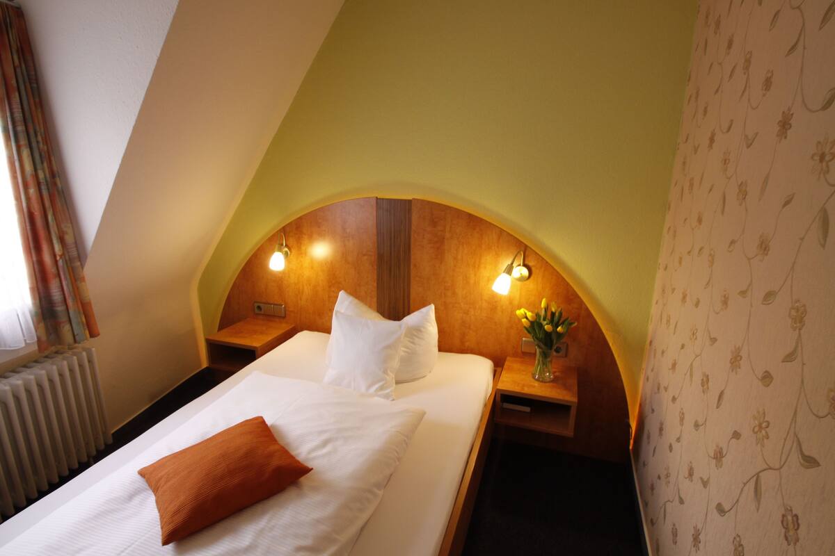 A hotel room with a bed, two bedside tables, a nightstand, a radiator, and a floral wallpaper.