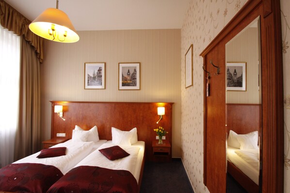 A hotel room with a large bed, two bedside tables, a nightstand, a mirror, and framed pictures on the wall.