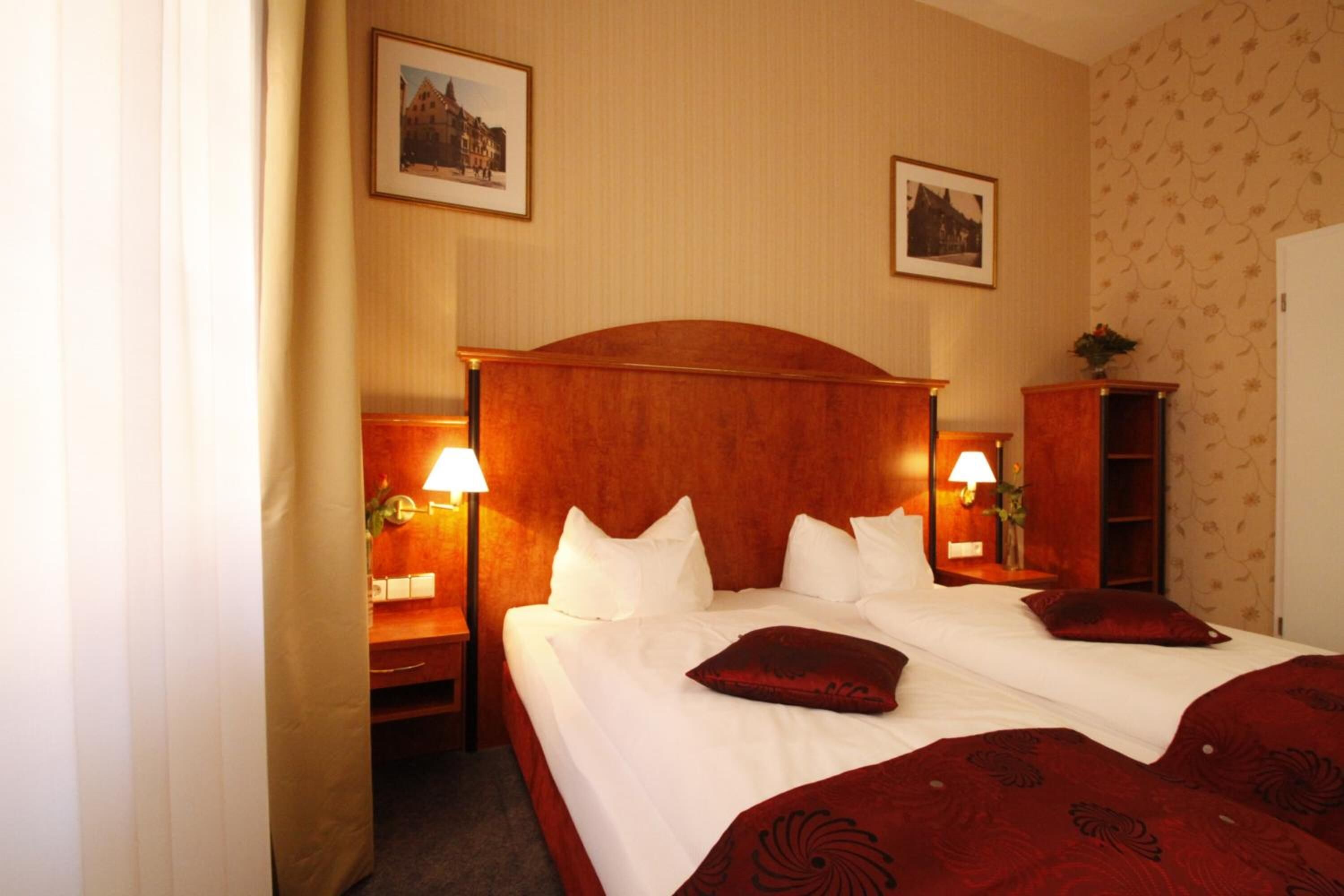 Een hotelkamer met een groot bed, twee nachtkastjes met lampen, een kledingkast en twee ingelijste foto's aan de muur.