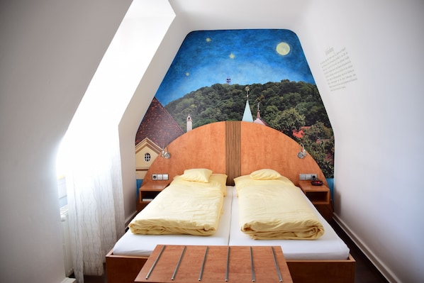 Un dormitorio con dos camas, un mural con cielo estrellado en la pared y una ventana pequeña.