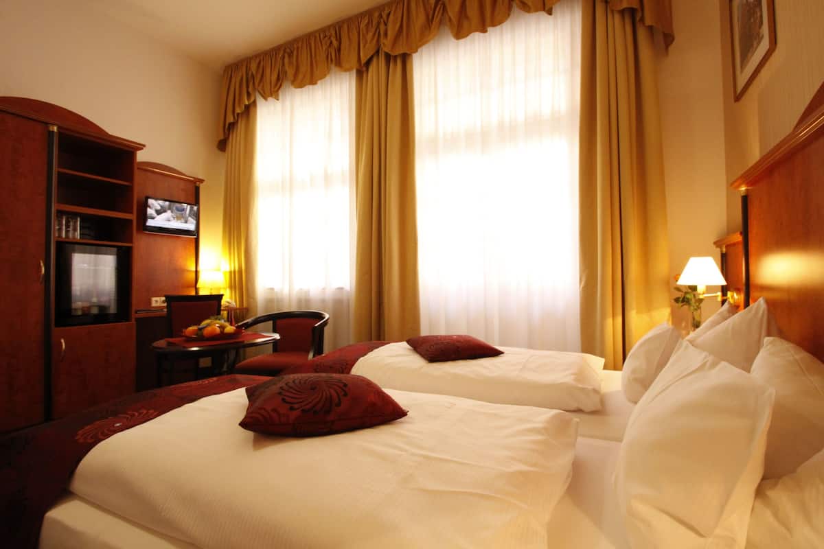A hotel room with two beds, a TV, a desk with a chair, and a minibar.