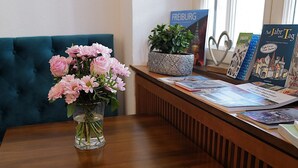 A wooden reception desk with a vase of pink flowers, a potted plant, and a display of travel brochures. - Hotel Barbara (Freiburg im Breisgau)