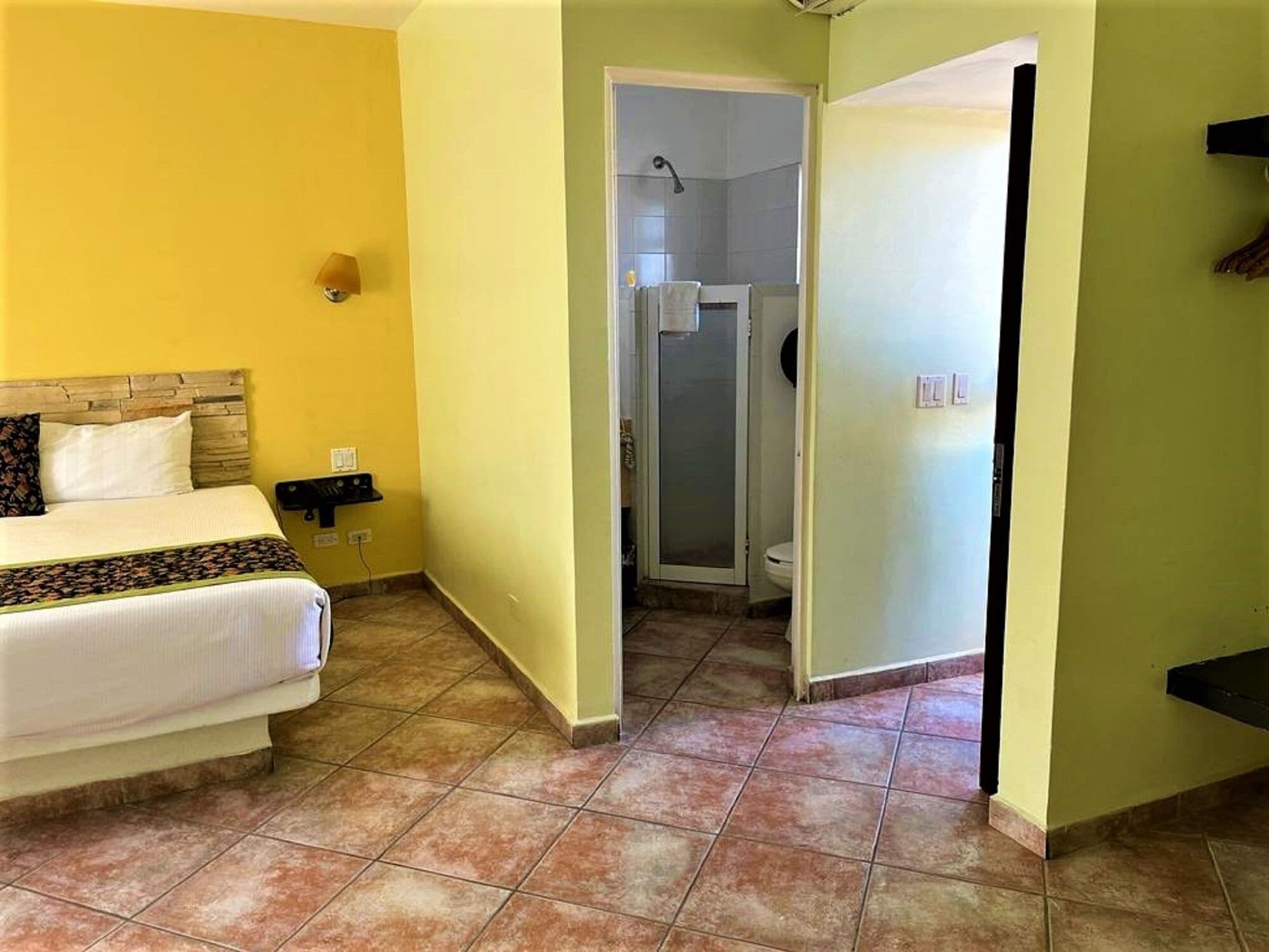 A hotel room with a bed, a small table, a shower, and a toilet.