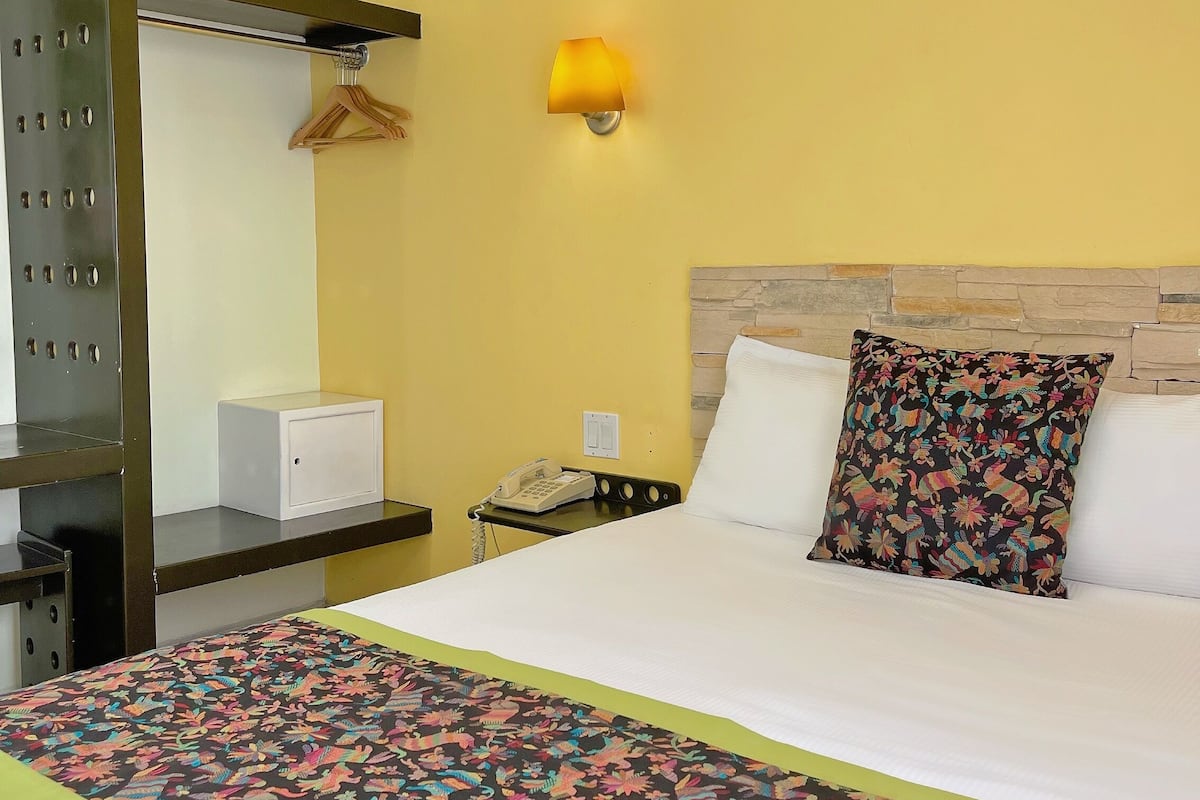 Une chambre d’hôtel comprenant un lit, une table de chevet avec un téléphone, une lampe fixée au mur, un porte-manteau et une armoire.