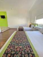 A hotel room with a large bed, a smaller bed, and a sofa. There is a window with a view of the outdoors.