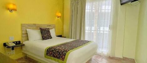 Une chambre d’hôtel équipée d’un lit, d’un bureau, d’un téléphone et d’un téléviseur fixé au mur.