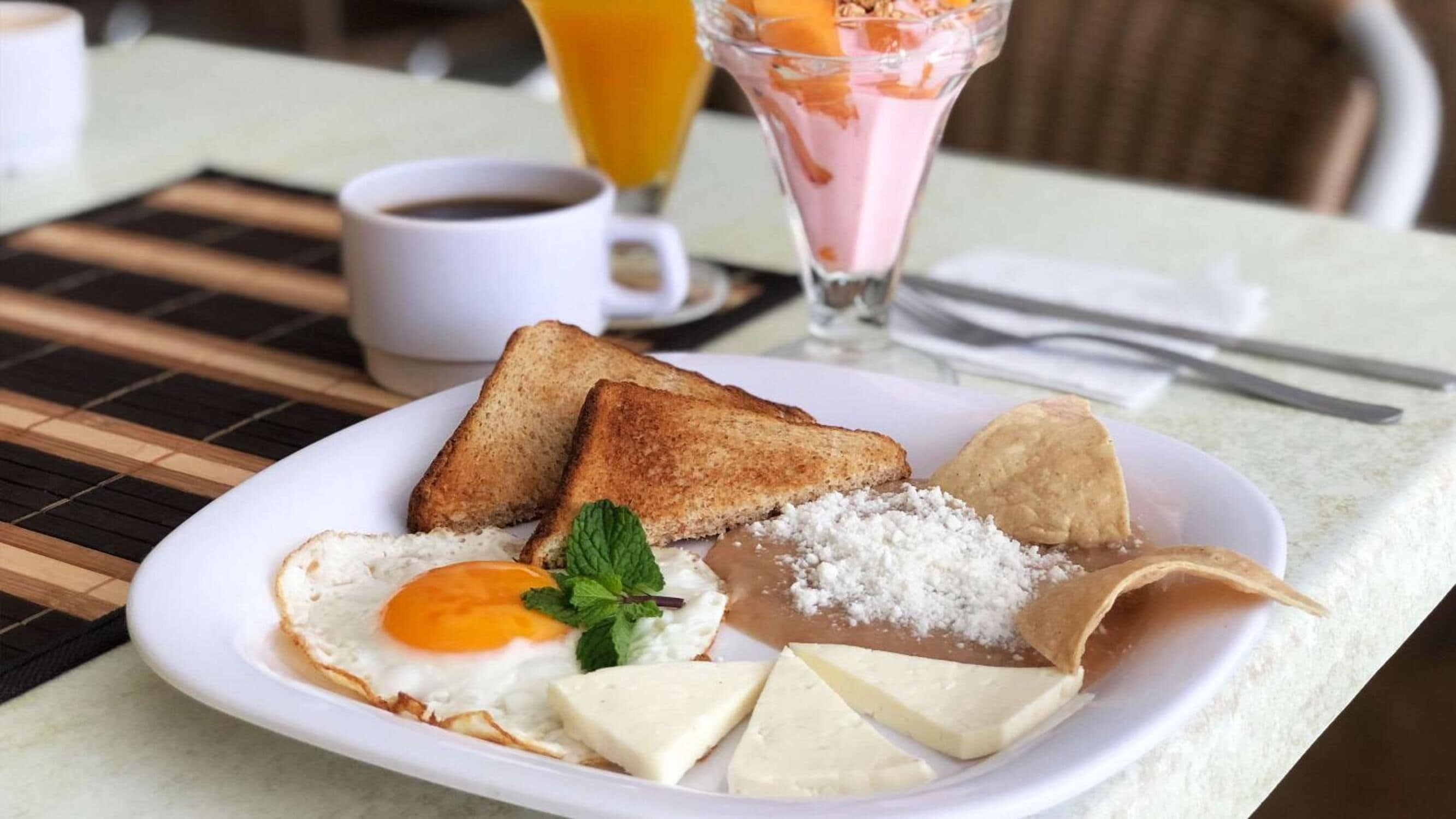 Une assiette de petit-déjeuner avec des toasts, des œufs, du fromage et un smoothie aux fruits.