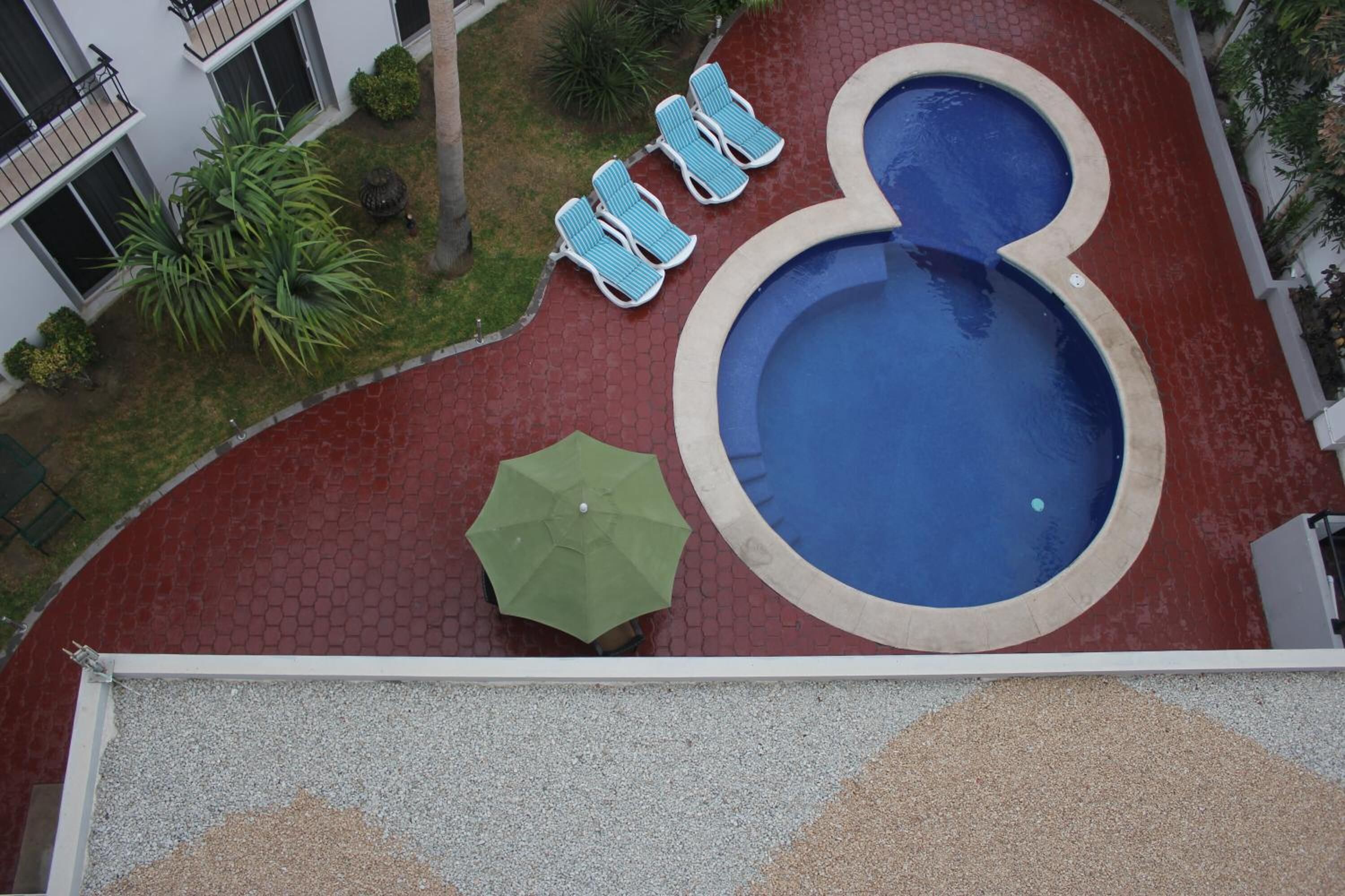 A rooftop pool with a circular edge, surrounded by a red tiled deck, and three lounge chairs with blue cushions.