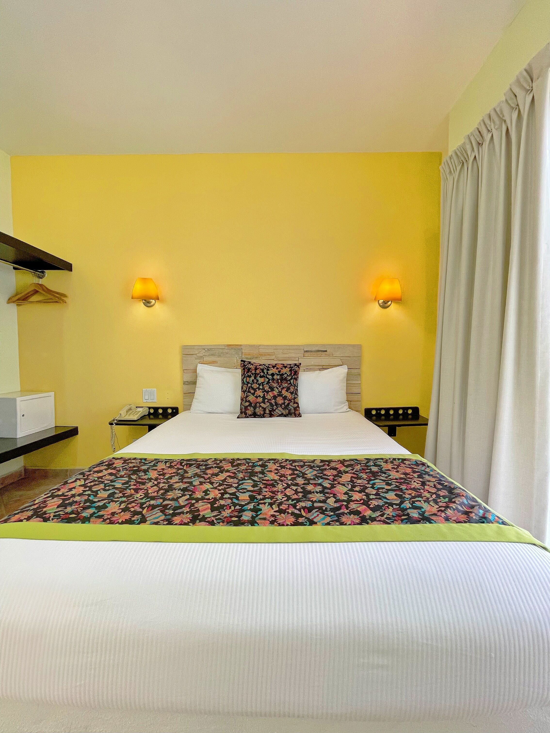 A hotel room with a bed, two bedside lamps, a telephone, and a desk with a lamp.