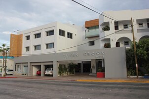 Un hotel moderno con un llamativo letrero que dice 'SEVEN CROWN HOTEL', una zona de estacionamiento techada y vista de la calle con vehículos estacionados.