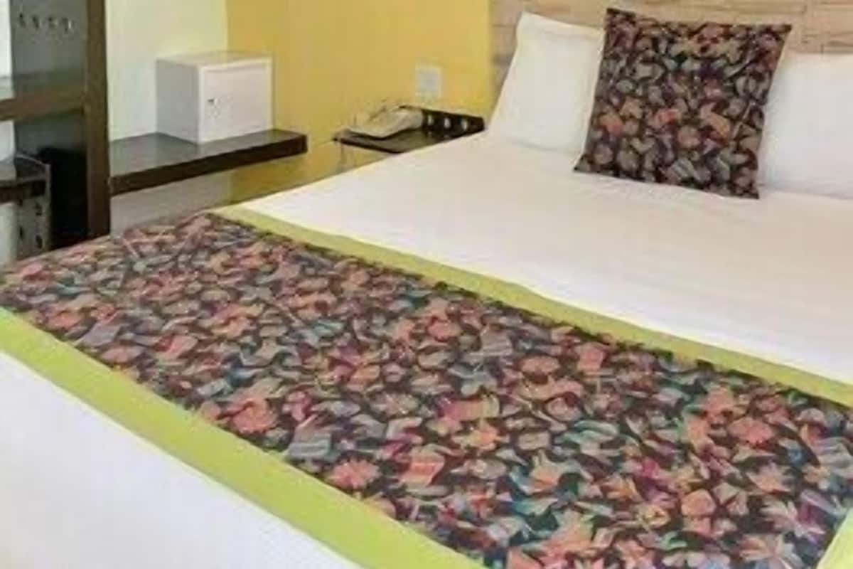 Une chambre d’hôtel comprenant un lit, une table de chevet, une lampe, une armoire et une étagère fixée au mur.