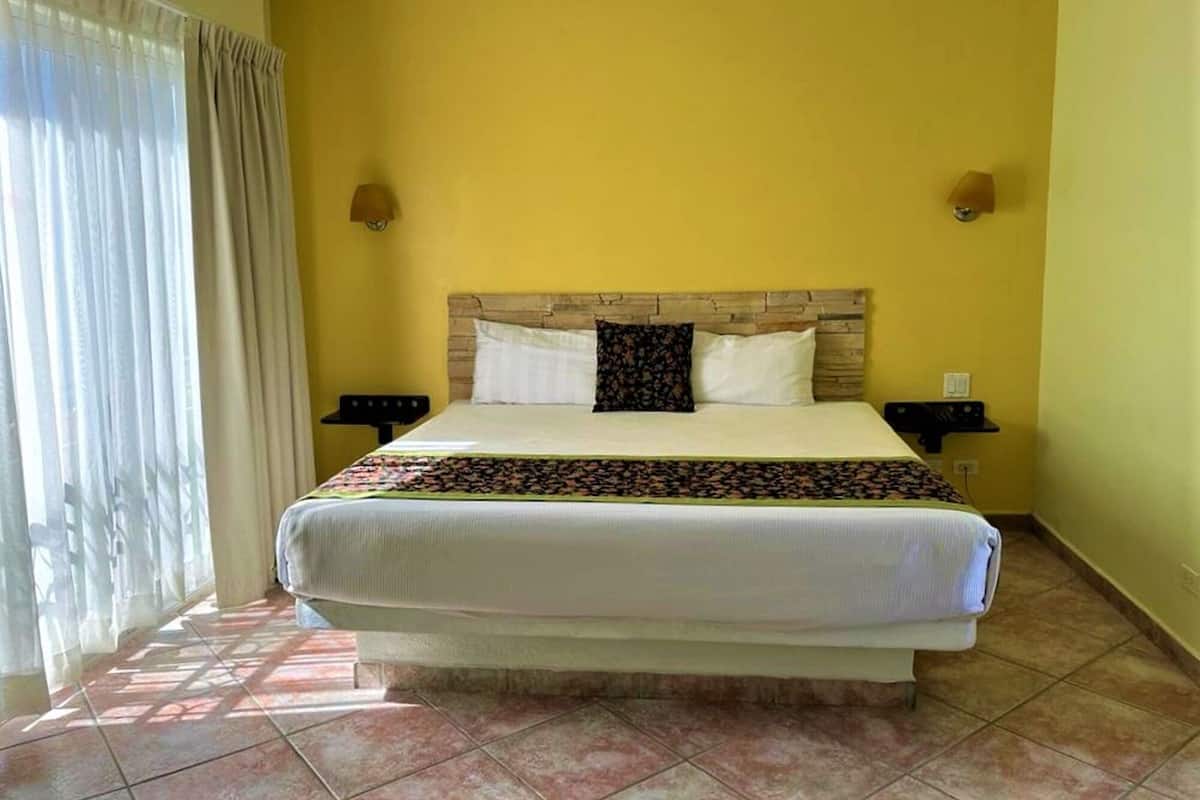 Une chambre d’hôtel avec un grand lit, deux tables de chevet, une tête de lit et une fenêtre avec des rideaux.
