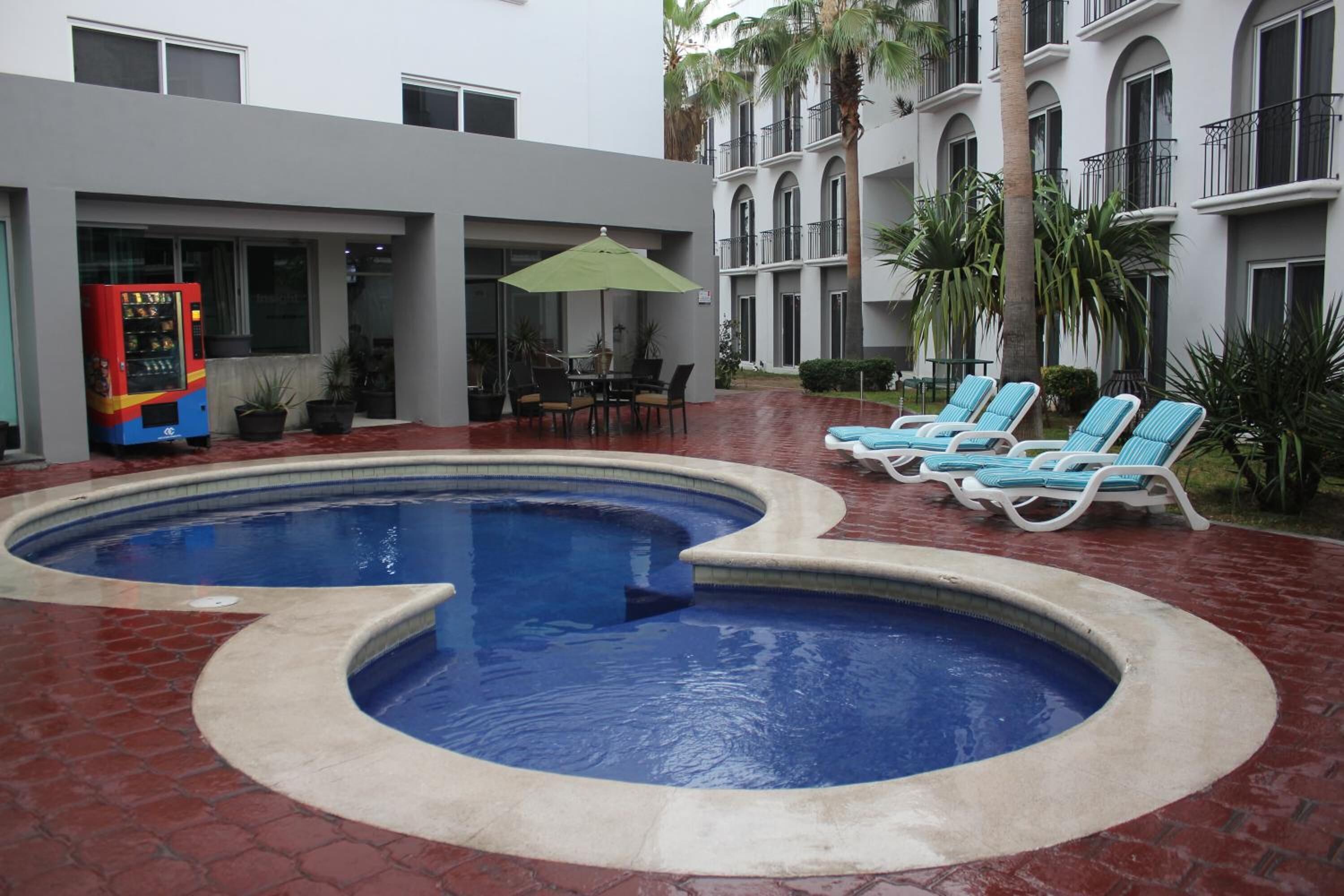 A swimming pool with a unique design, surrounded by lounge chairs and a vending machine.